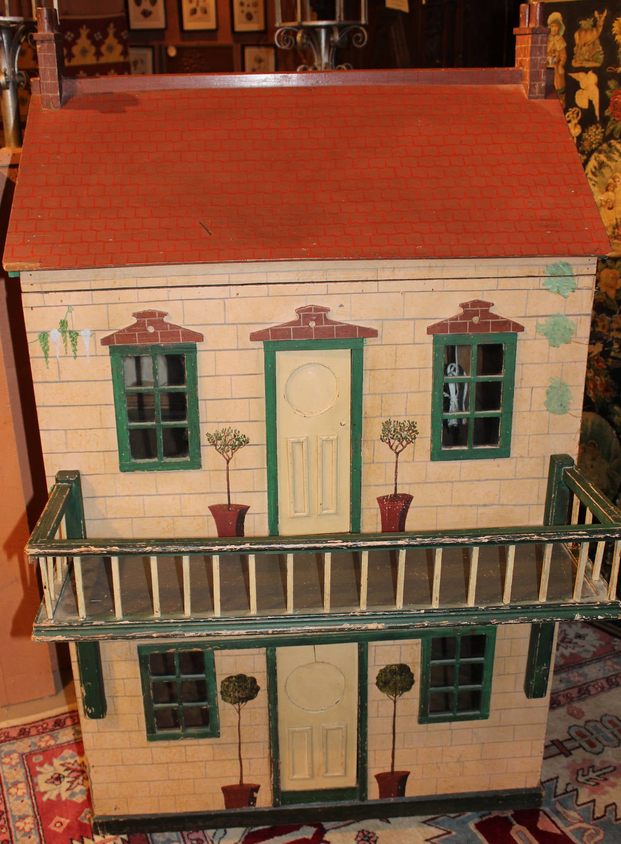 A large handmade and painted wooden two-floor doll house, probably early 20th century English,  with veranda on the top floor, and hinged front which opens to expose the two interior rooms. Traces of the original wallpaper remain on the walls, with