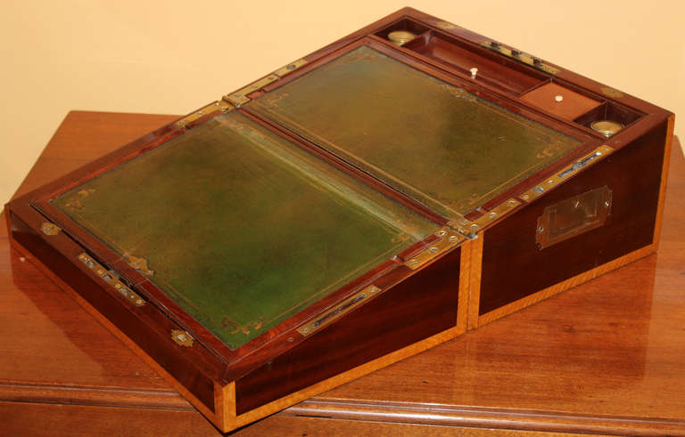 Fine English ship captain’s writing box or lap desk featuring brass handles, satinwood edges, lift out writing box, two inkwells, green leather writing surfaces, and includes a secret compartment which opens by pressing the false hinge screw. 19th