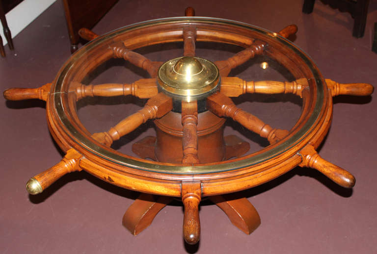 19th century ship wheel with brass nave featuring nicely turned spokes and handles, one with brass cap. The wheel has been mounted on a columnar base and has a glass top making it a perfect coffee or side table.