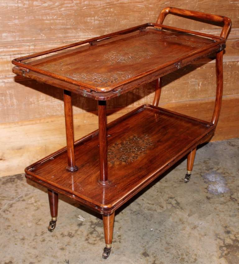 A fine Mid-Century aesthetic copper and brass inlaid tea cart or side table. The two galleried trays connected by a bentwood handle and all raised on four tapered legs terminating in brass casters. Wonderful patina.