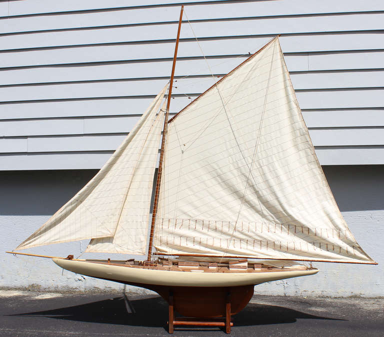 Mahogany pond boat with cream color painted trim with off-white canvas sails, rigging, and deck detail, and one rowboat or lifeboat.