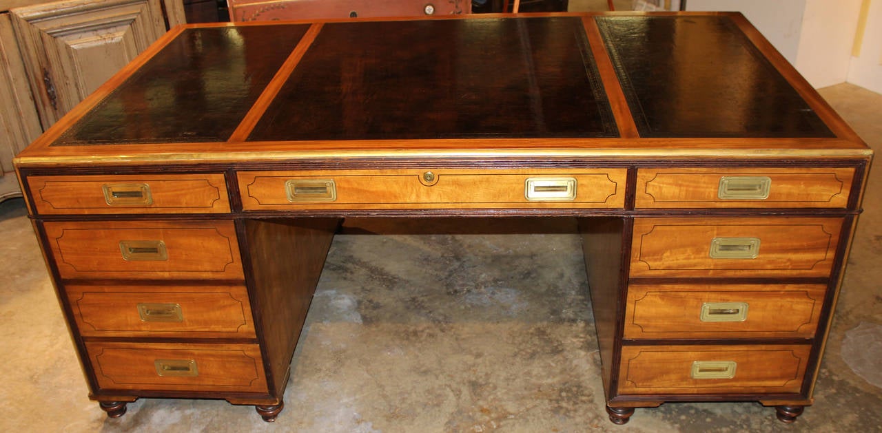 A Campaign-style three-panel tooled leather top mahogany and satinwood partners desk by Baker Furniture, with recessed brass hardware and trim, turned feet and reeded mahogany banding. Baker Furniture label appears inside the top drawer, circa