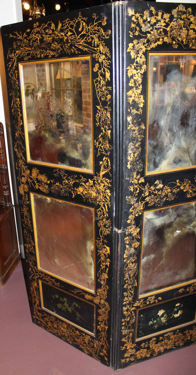 A beautiful 19th century black lacquer three section mirrored screen, with naturalistic gold gilt decoration. Each section has two fitted mirror plates, with the lower panel of each showing polychrome floral decoration.