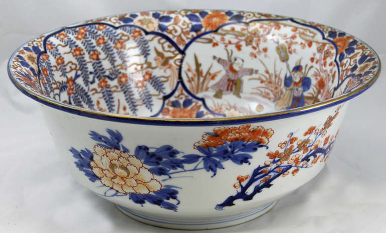 A 19th century large Japanese Imari bowl with flared lip, with alternating foliate and figural interior panels, on a foliate background with gilt gold highlights.  The exterior of the bowl continues the foliate decoration on the white background.