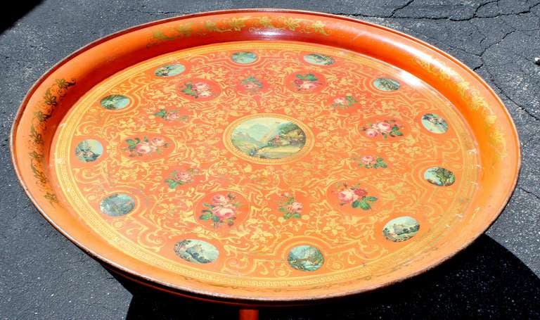 Superb large round tray table with polychrome decoupage and gilded stenciling on a brilliant orange ground.  Decoupage cartouches depict Swiss scenes alternating with rose vignettes.  Gilded designs include foliate, scrolls and Greek key.  Glass top