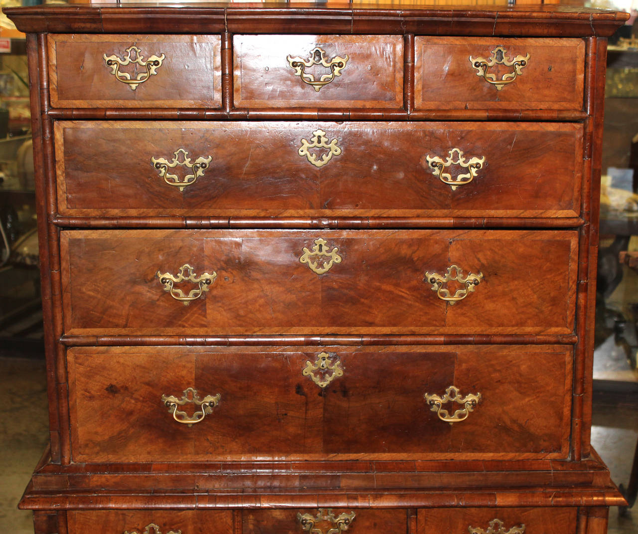 An 18th century English high chest or highboy in burled and banded veneer, cabriole legs terminating with hooves, and a nicely carved apron. The top show three small fitted drawers over three large drawers. The base shows one small fitted center