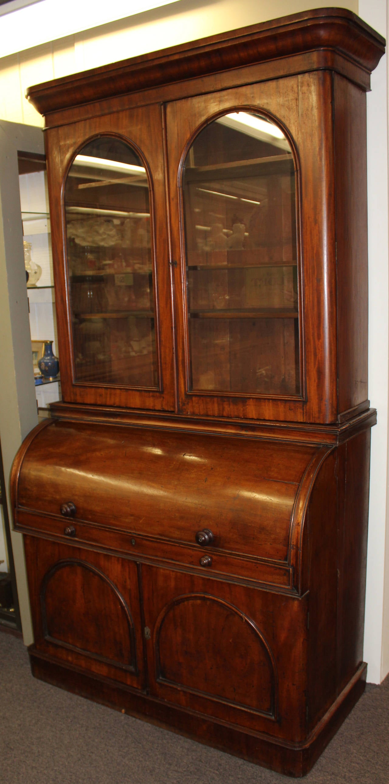 A 19th century two part walnut English cylinder secretary desk and bookcase with nicely compartmentalized interior featuring a sliding writing surface with tooled leather and well chosen burled veneers. The two glazed arched doors in the upper