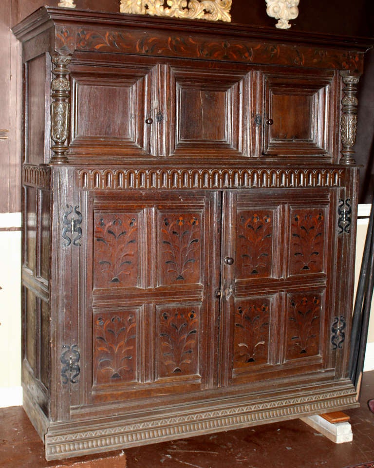 This large 17th century English court cupboard is decorated with floral inlay on the paneled doors and top frieze. 

This piece was adapted and incorporated into a custom larger built-in bookcase at its previous home. The back panels have been cut