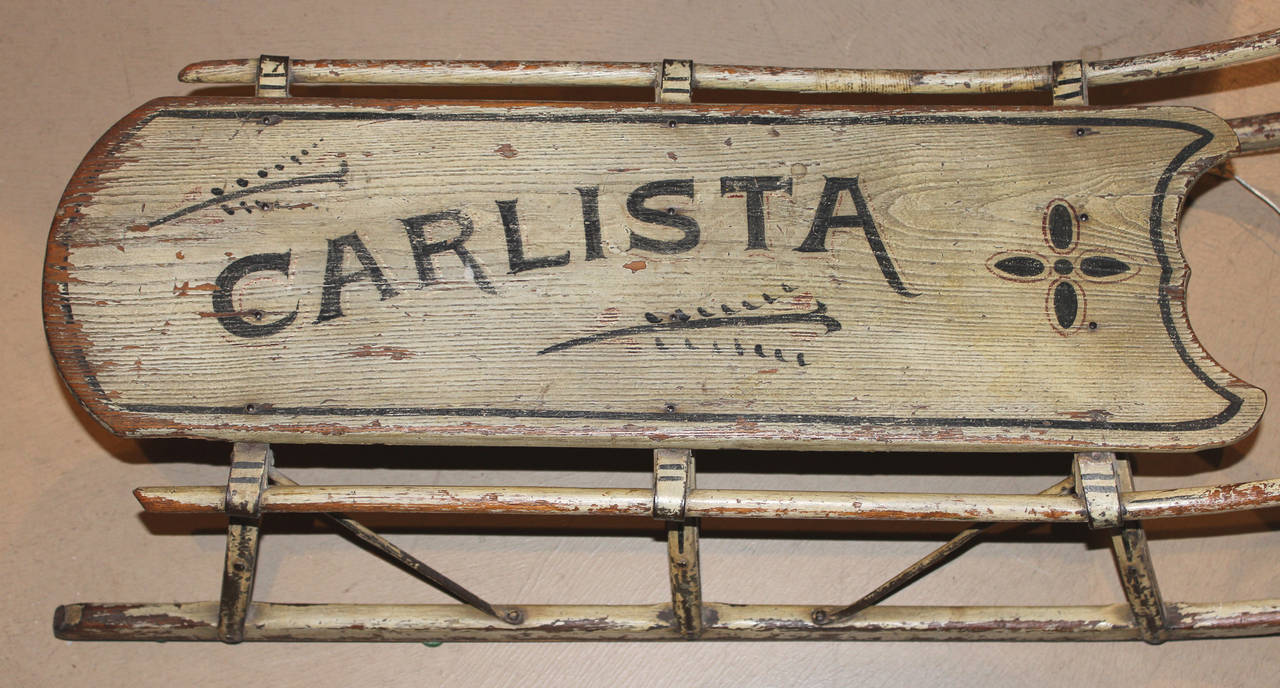 A 19th century child’s sled in original white paint with wooden supports and rails with iron runners. Boldly decorated with child’s name “Carlista”.