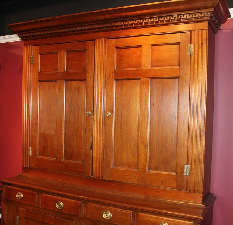 An exceptional two-part walnut Pennsylvania cupboard or hutch, the upper section with paneled doors revealing two shelves. The lower section fitted with four drawers and paneled doors over a bracket base. Dentil molding, fluted stiles and brass
