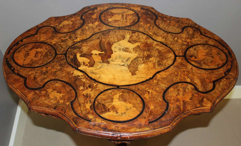 This wonderful late 19th century burled walnut German Black Forest Tilt Top Table is inlaid on the top with several vignettes of animals, including deer, ram, sheep, and rabbits, along with foliage. The tripod base is exquisitely  carved with