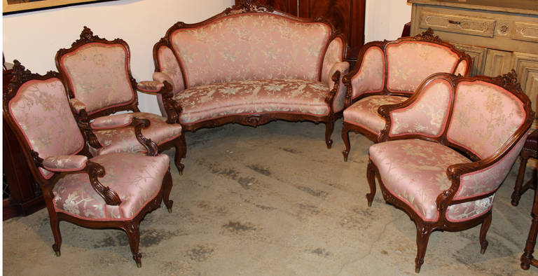 This nicely upholstered 19th century French fruitwood salon set includes a settee, two bergere chairs, and two arm chairs. Each piece is beautifully hand carved with pierced leaf and scrollwork.