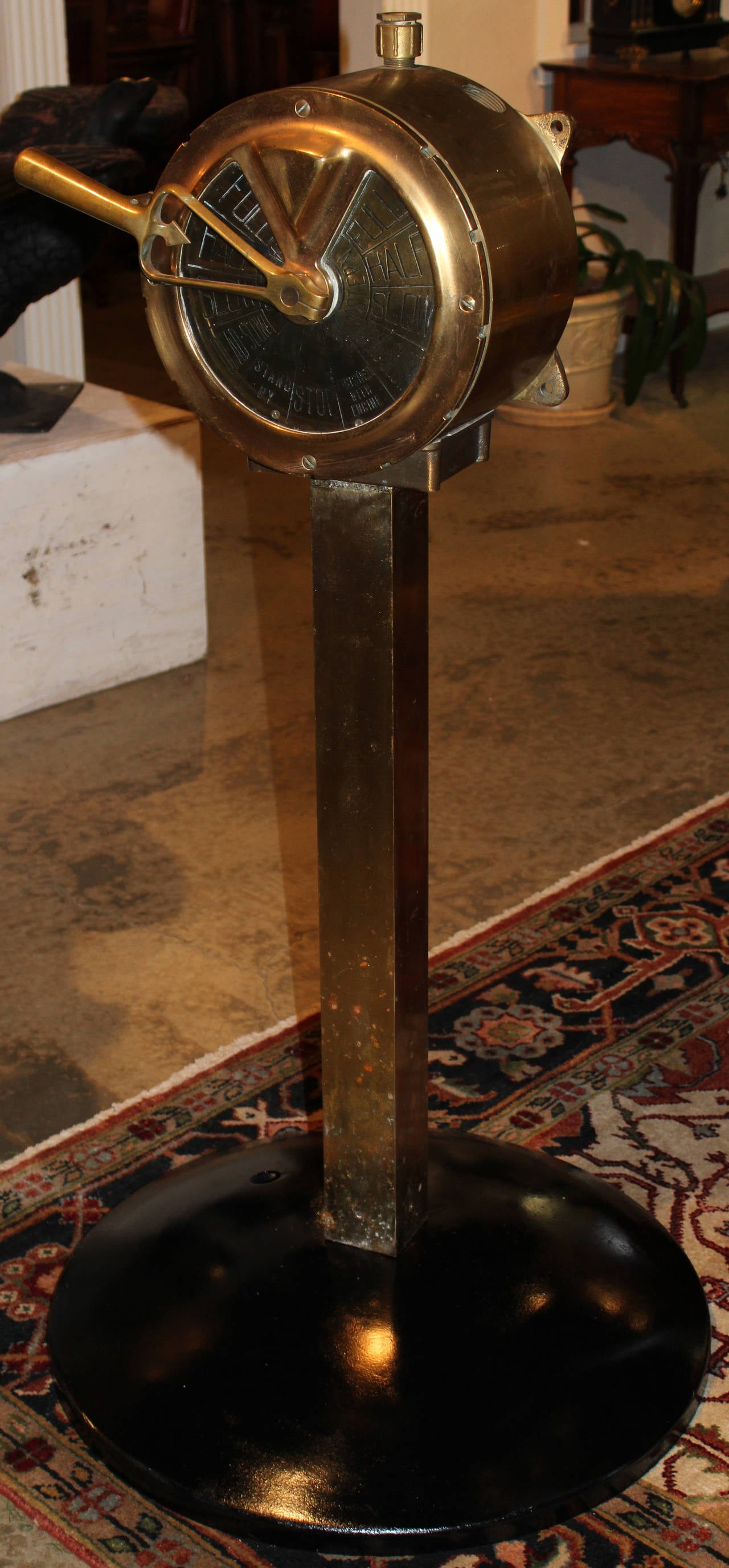 A brass ship’s or engine order telegraph, mounted on a square brass post and all supported on a later base enabling it to stand freely. The bottom of the telegraph face is marked CX-109. A telegraph with a single handle reflects a ship with a single