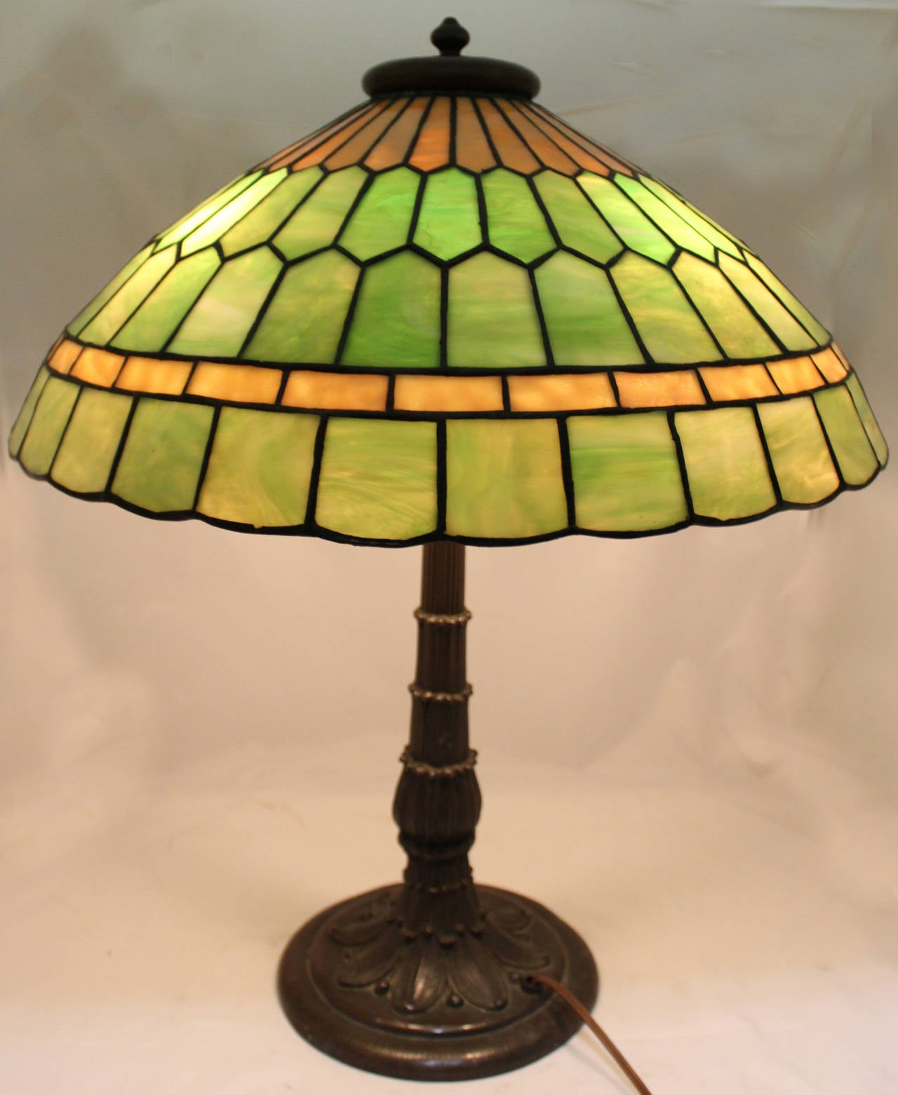 This exquisite Arts & Crafts leaded stained or slag glass lamp with heavy bronze acanthus decorated base dates to the early 20th century, similar in style and quality to Duffner & Kimberly.