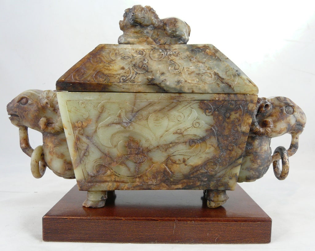 Magnificent covered jade incense burner carved of olive-green, semi-translucent jade with strong russet inclusions.  This archaic-form piece features 2 large rams' head handles with loose jade rings and a recumbent ram on the cover.  All surfaces