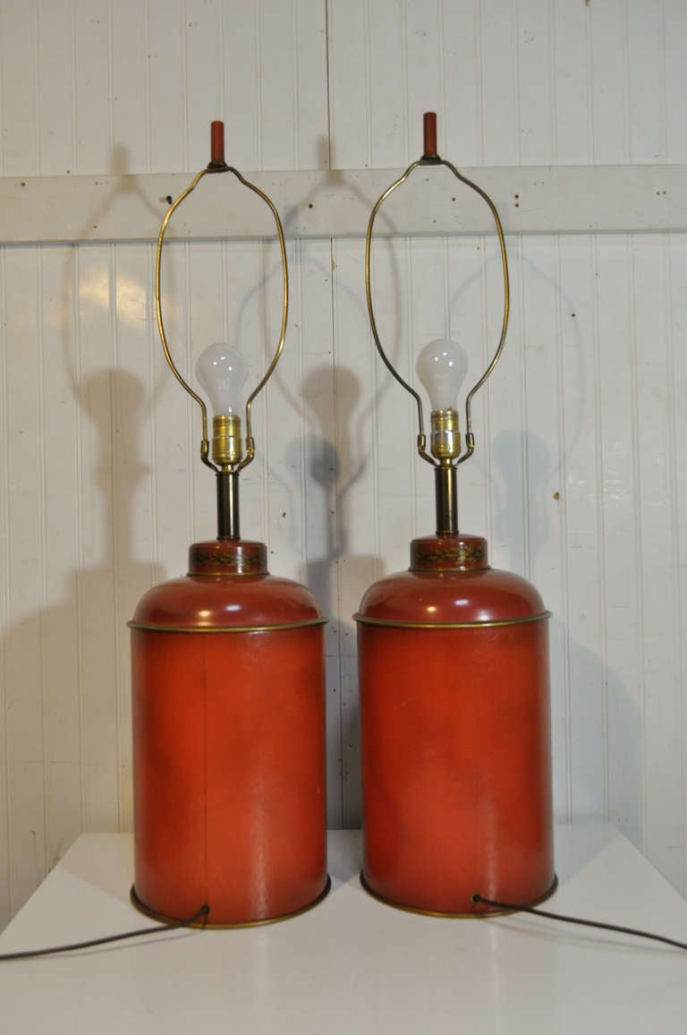 Early to Mid 20th Century pair of vintage French style burnt orange tole metal and leather wrapped English tea canister shaped lamps. The lamps feature a French lion and unicorn coat of arms decoration on the face, and a foliate decoration around