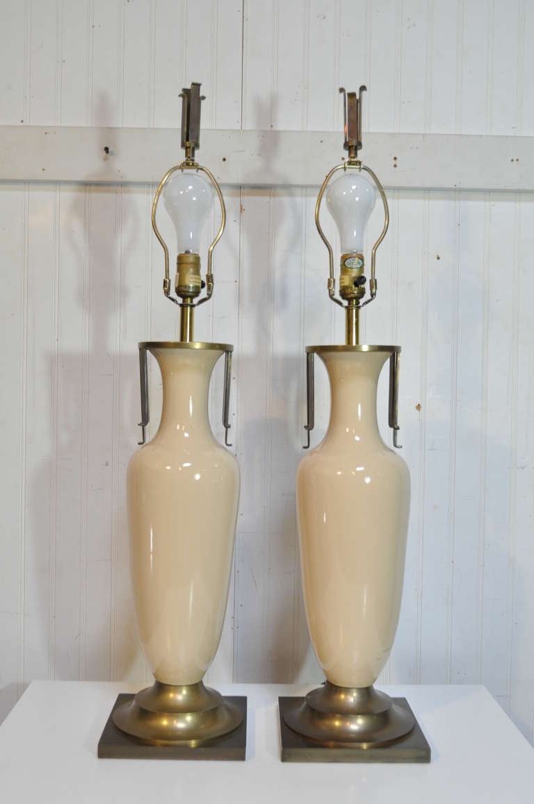 Glamorous Pair of vintage Hollywood Regency ivory glazed urn form ceramic table lamps. Both the bases and finials are brass. Labels on sockets are marked © 1985 Chapman. Sockets are 3-way. The style is very similar to the works of Dorothy Draper