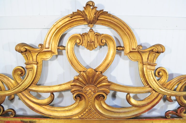 Stunning Vintage Antiqued Gold Gilt Carved Wood King Size Headboard. Item features a stately hand carved wood frame, antiqued gold gilt and gold leaf detail, ornate pierced design, iron supports at the rear, and flashy french Hollywood Regency form.