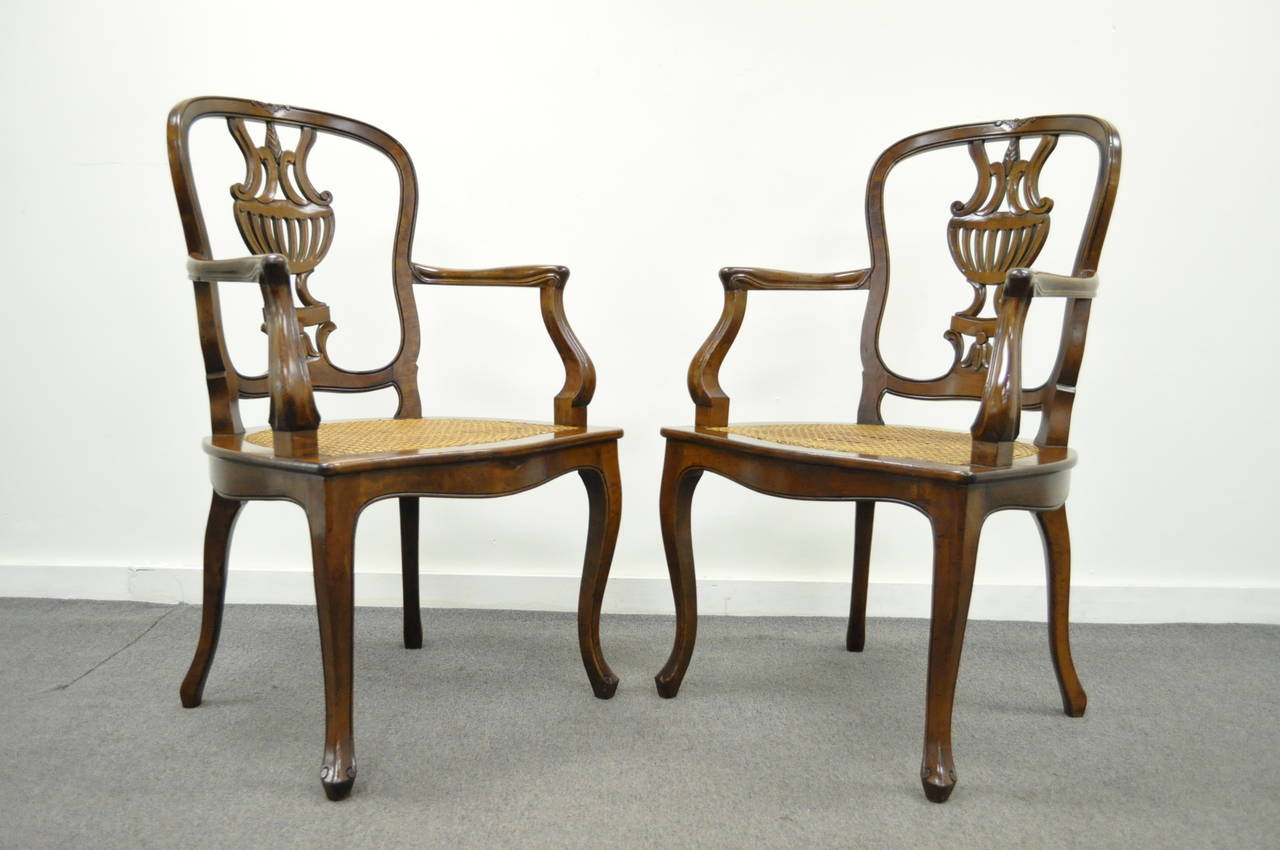 Stunning pair of solid walnut, distress finished, hand-carved armchairs in the Rococo taste. The pair features shapely carved, urn form, backsplats, cane seats, cabriole legs, and a desirable and original antiqued finish. Made in Italy stamp on the