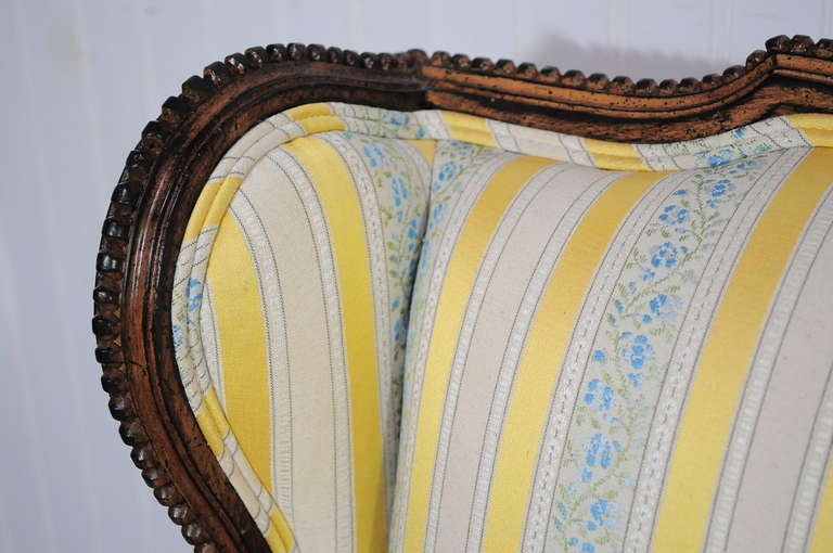 Vintage French Louis XVI Style Wing Back Settee designed by Lewis Mittman Inc. This item features a beautifully carved antiqued finish solid wood wing back frame, reeded and tapered legs, upholstered armrests, and beautiful gold striped fabric with