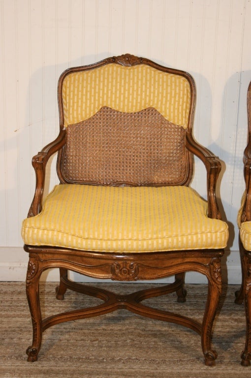 Great Pair of Vintage French Style Carved Open Arm Chairs with unique x-form stretcher bases. This fantastic pair of chairs features beautiful carvings on the frame, caned back and seats, and removable padded seat cushions with padded armrests. Each