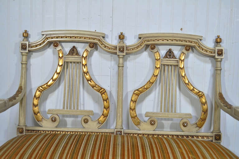 Beautiful vintage 1940s cream and gold gilt finish French neoclassical/Louis XVI style lyre back settee / two seat loveseat. Item features a finely carved solid wood frame, gold gilt acanthus and floral accents, fluted column form legs, carved