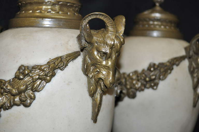 Gorgeous pair of French Louis XV / Neoclassical style urn form marble and bronze figural cassolettes. Item features decorative bronze ram's head ormolu, draped floral acanthus, a smaller foliate insert toward the base. Very nice and attractive pair