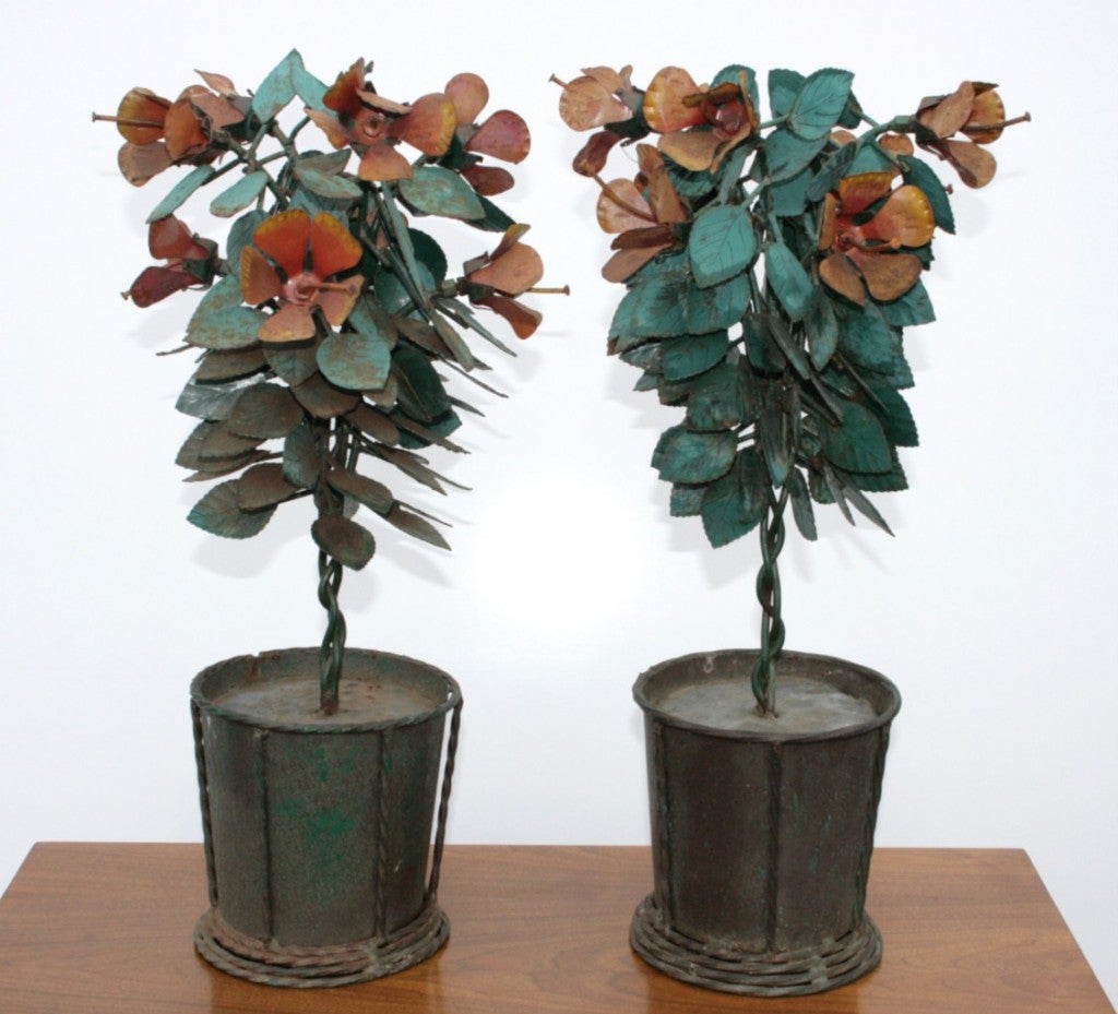 Pair of 24 inch tall vintage artisan crafted modernist tabletop planter sculptures in iron. Sculptures feature hand-painted green leaves, orange and yellow flowers all resting in iron planter pots. Finish has achieved a desirable rusted and aged