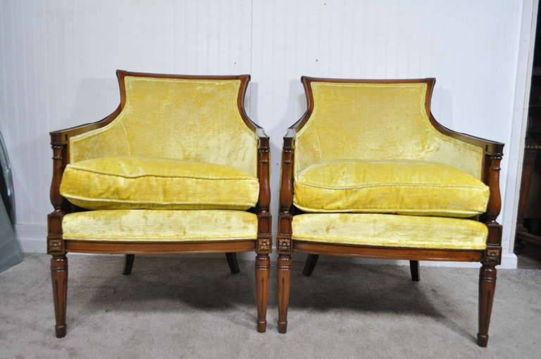 Pair of stylish vintage French Hollywood Regency style yellow fireside armchairs. The chairs feature a very nice sinuous form with carved florets at the joints, fluted legs, and lightly distressed original finish.