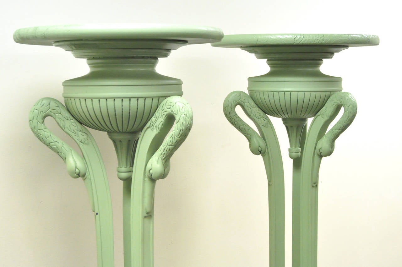 Pair of tall and stately vintage neoclassical style pedestals with urn form capitols atop a tripartite swans head and hairy hoof foot base. The pedestals are comprised of molded fiberglass and wood, finished in a matte green lacquer.