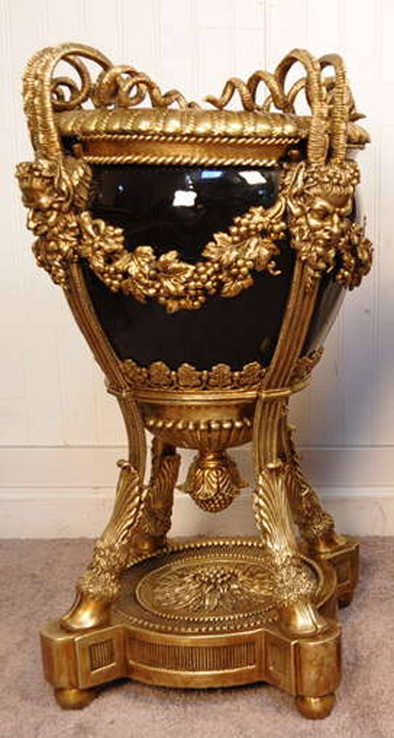 Breathtaking bronze and black porcelain figural urn or planter in the French Empire or Louis XVI taste from the late 20th century. The piece features scrolling horned faces, hairy hoof feet, grape vine draped wreaths, acorn finials and a fantastic