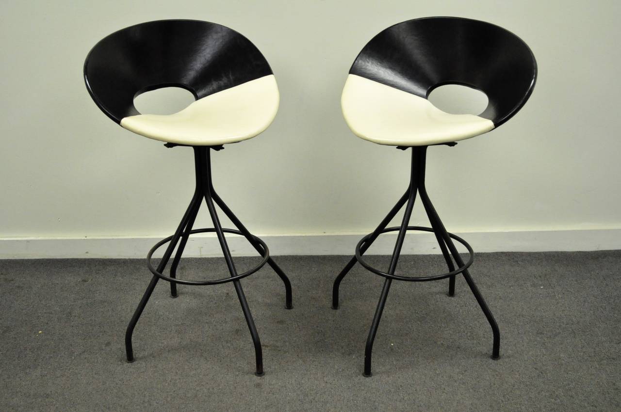 Pair of striking original mid century modern, circa 1950's, iron & vinyl swivel bar stools. The chairs feature a decidedly Italian flair, with wide black and cream colored vinyl wrapped seats, and dramatically splayed black wrought iron legs.
