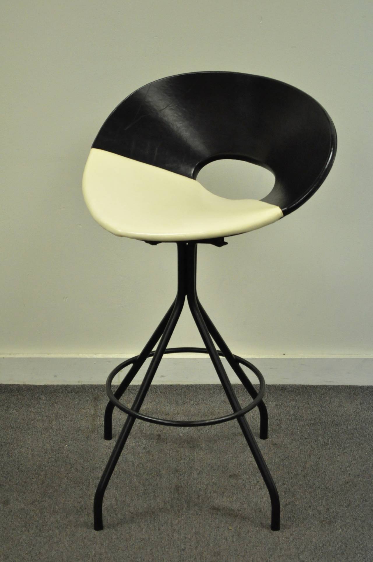 A striking original mid century modern iron & vinyl wrapped swivel bar stool. The chair features a decidedly Italian flair, with a wide black and cream colored vinyl seat, and dramatically splayed black wrought iron legs. Exemplary mid century