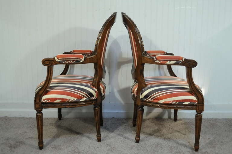 High quality pair of carved wood French armchairs in the Louis XVI taste with newer regal striped upholstery. Item features delicately carved solid wood frames, tapered reeded legs, medallion backs, upholstered armrests, and Classic Louis XVI French