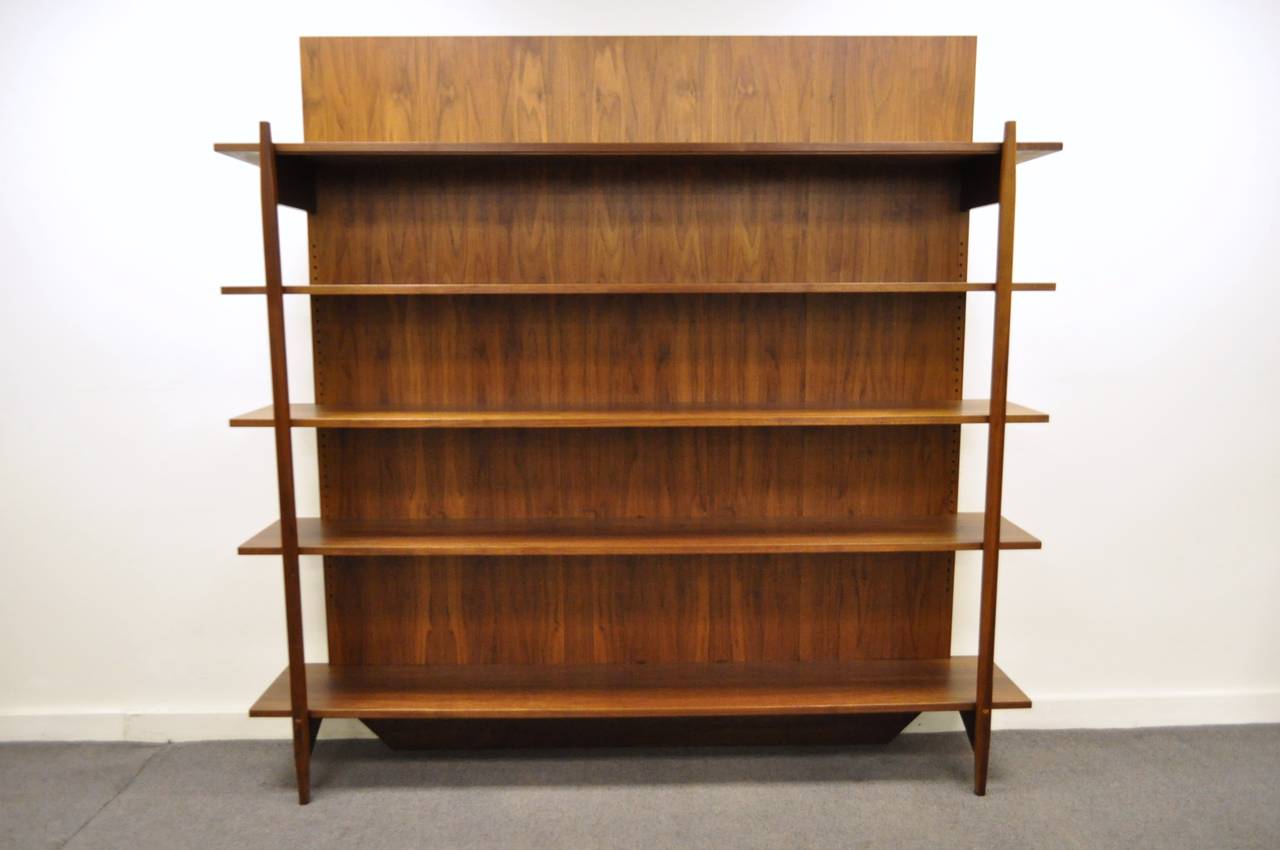 Large and impressive custom made teak veneer bookcase or wall unit in the Danish taste. The piece has a very sleek minimalist design, and a truly beautiful and rich wood grain. Though the back has peg holes, the shelves are fixed in place by both