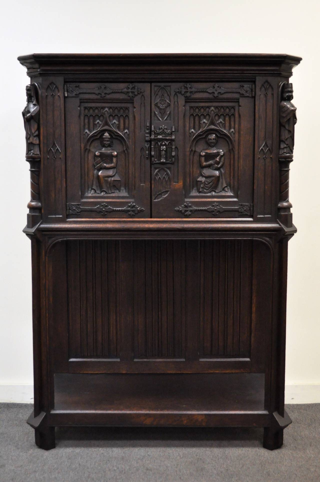 Hand-carved solid oak Renaissance / Gothic Revival cabinet Made in Belgium. The cabinet features carvings of several figures in relief surrounded by carved Gothic style architectural elements. The doors have large sculptural leaf form cast iron