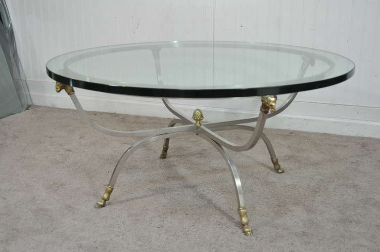 Remarkable high quality vintage Italian rams' head & hoof foot brushed steel and brass Neoclassical Style circular coffee table with a thick .75" glass top. The piece features a classic X-form stretcher base with solid cast brass rams' head