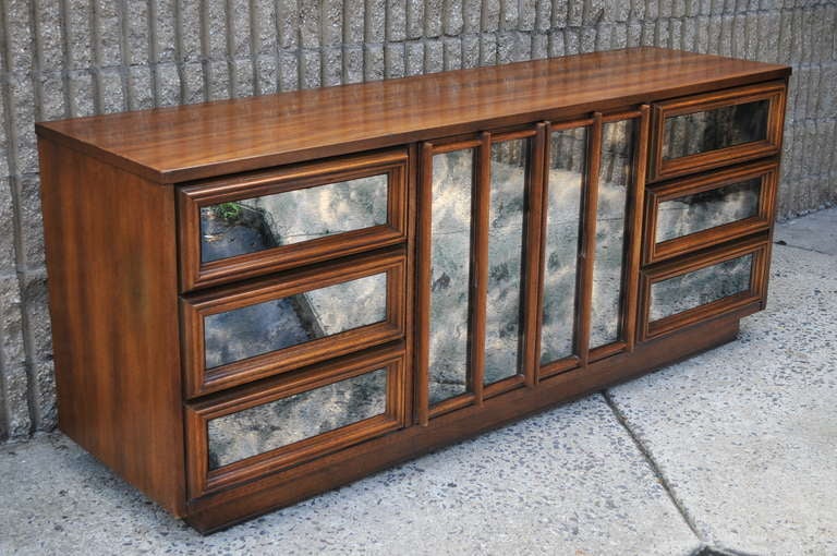 Very unique vintage long dresser with antiqued/smoky mirror fronts and hidden pulls for a great sleek modernist form. There are a total of 9 dovetailed drawers with three hidden drawers behind the mirrored center double door fronts. This great piece