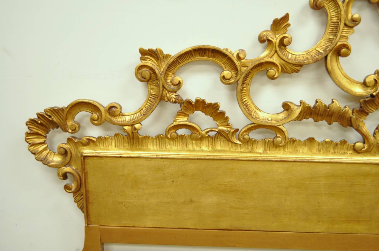 Very ornate and richly carved wood king-sized bed headboard in the French Rococo / Hollywood Regency taste. The piece features very thickly carved scroll and acanthus motifs, and a very striking gold gilt finish. The carved portions are reinforced