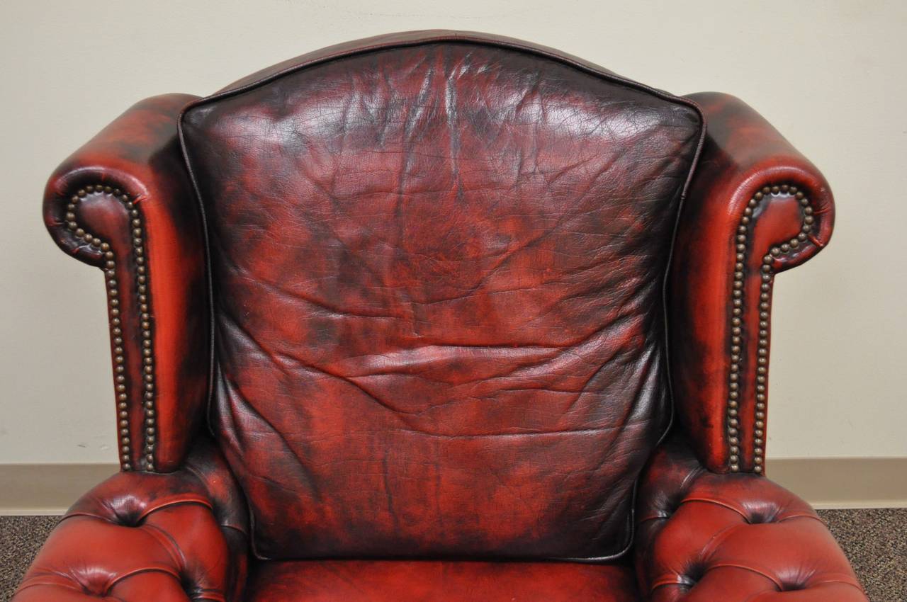 A very impressive and stately vintage, Chesterfield style armchair. The piece features dramatically rolled arms and wings in the English taste, a nicely sloped Silhouette, red antiqued leather upholstery and traditional brass nailhead trim on