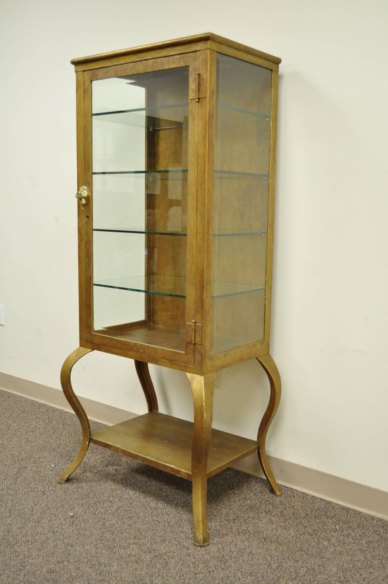 Vintage Metal Dental Cabinet Circa early 1900's. Cabinet features a painted steel case having a glass swing door and glass sides all of which are nicely beveled and open to four thick glass shelves. This medical cabinet is raised on shapely,