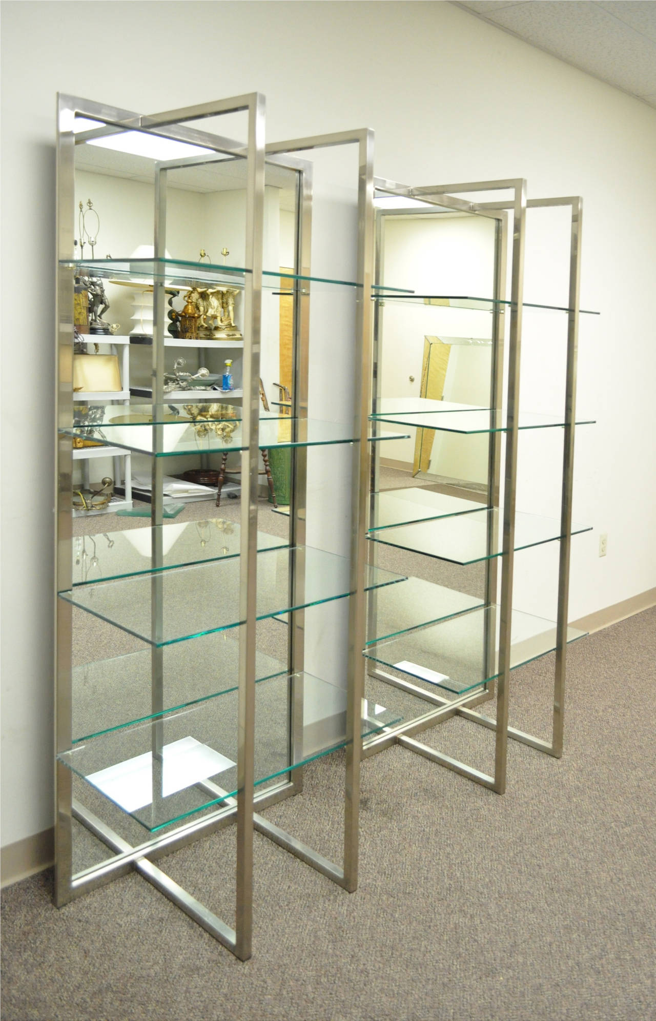 Pair of striking sculptural brushed steel étagerés. The pieces feature very uniquely shaped brushed steel frames, mirrored backs and four thick clear glass shelves each. Though the maker is unknown the cases have a great look, very reminiscent of