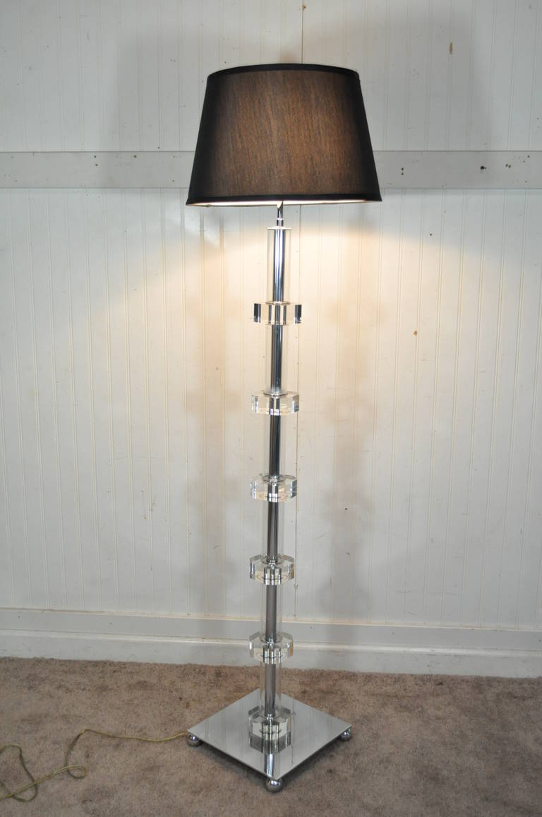 Very unique pair of Lucite and chrome floor lamps in the manner of Karl Springer. The pair features stacked Lucite shafts, with Lucite cylinders encasing the chrome interior shafts. The square chrome bases rest on four ball form feet. Each lamp has