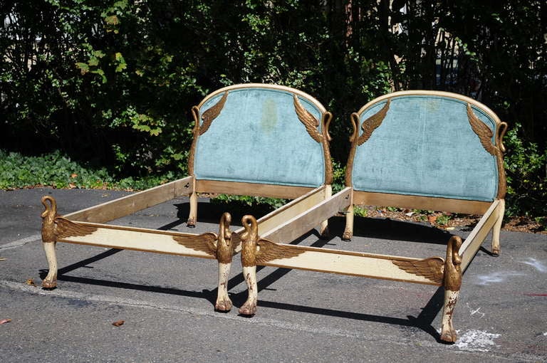 Remarkable pair of antique carved swan form French Empire / Regency style single / twin beds in the manner of Maison Jansen. This fantastic pair features distress painted cream and gold gilt finish, ball and claw feet, blue upholstered headrests and
