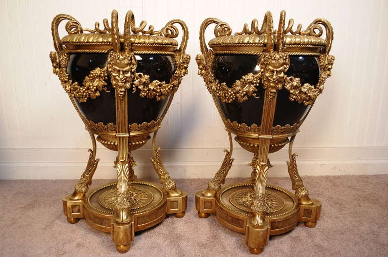 Breathtaking Pair of Bronze and Black Porcelain Figural Urns / Planters in the French Empire / Louis XVI Taste from the Late 20th Century. The pair features scrolling horned faces, hairy hoof feet, grape vine draped wreaths, acorn finials, and