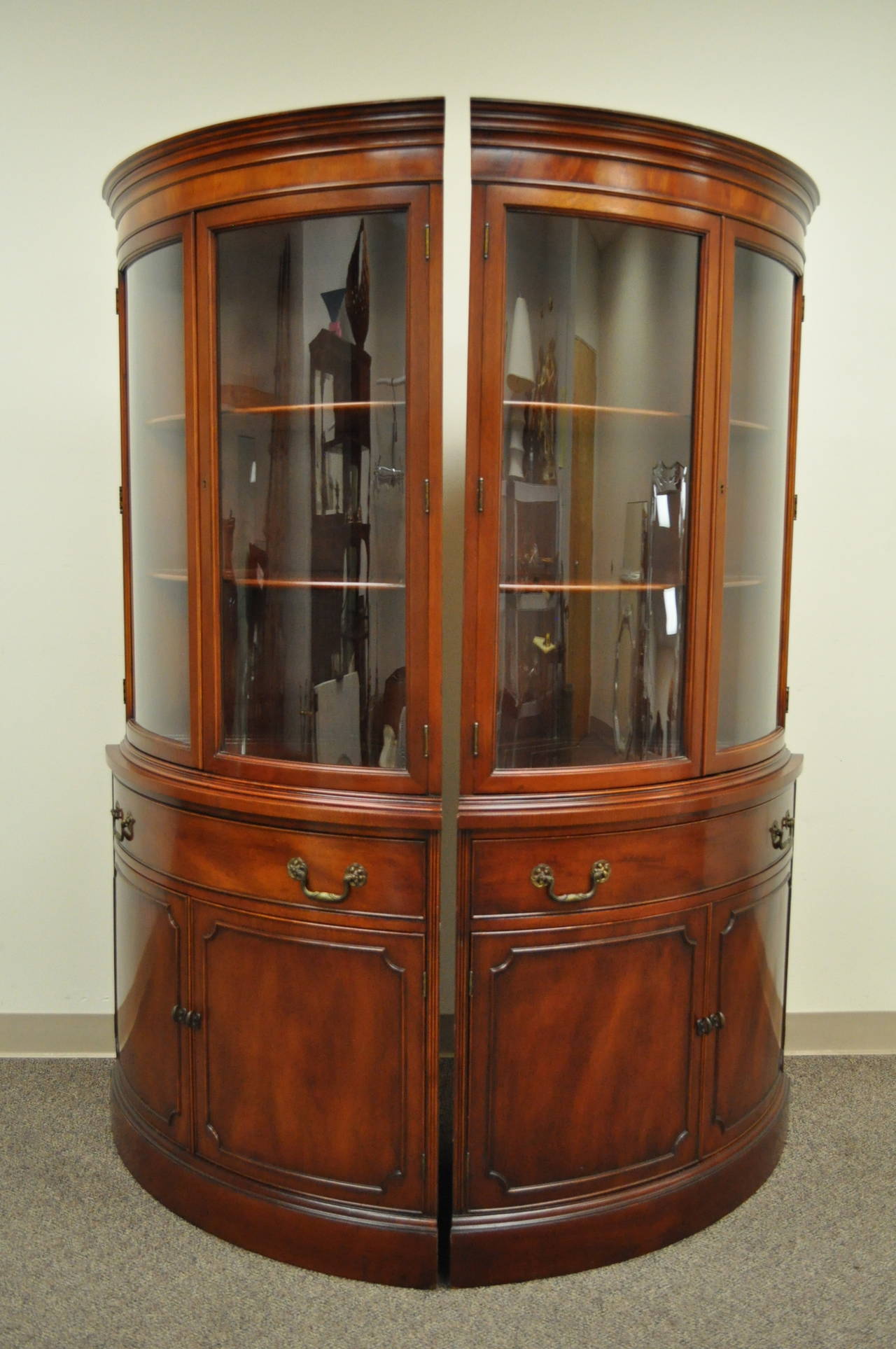 Beautiful pair of Mahogany demilune shaped corner china cabinets / cupboards. The pair features two curved glass swing doors, single drawer, lower swing cabinet doors with interior shelf, beautiful woodgrain throughout, and elegant and functional