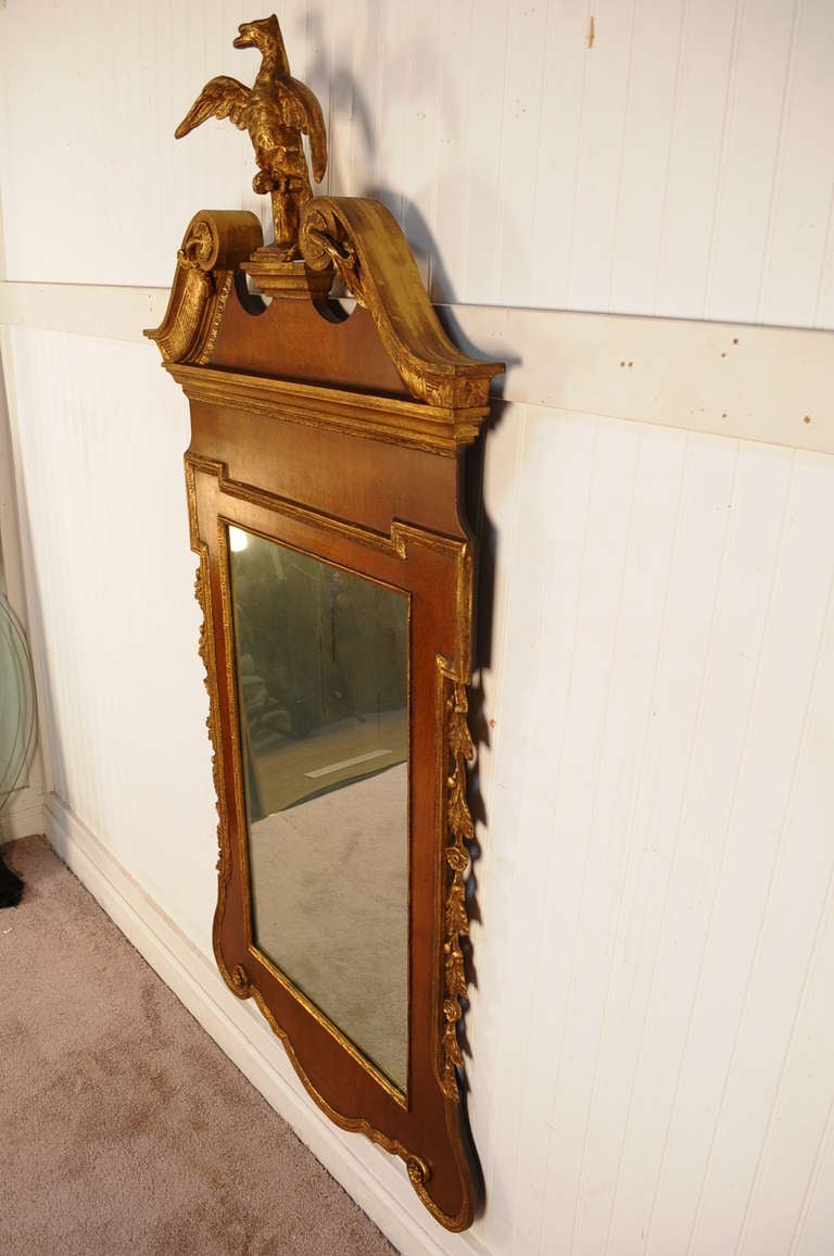 Stately Early to Mid 20th Century George III Style Wall Mirror with Gilded Eagle Crest by Friedman Brother. The mahogany and gold gilt frame is nicely carved while surrounding the antiqued/distressed mirror.