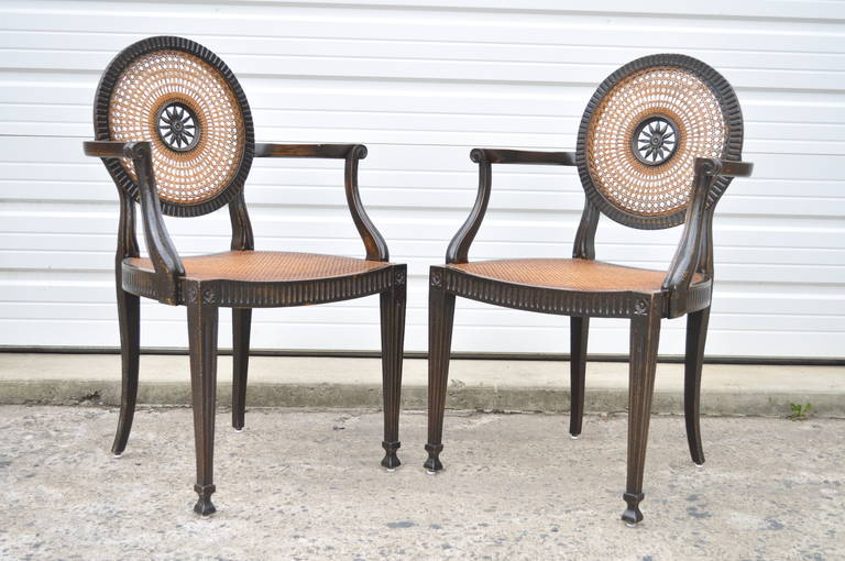 Elegant pair of vintage Italian made, hand carved and distressed, caned armchairs in the French Neoclassical / Louis XVI taste. Chairs feature caned backs and seats, carved wood sunburst central medallion at the backrest, reeded and tapered legs,