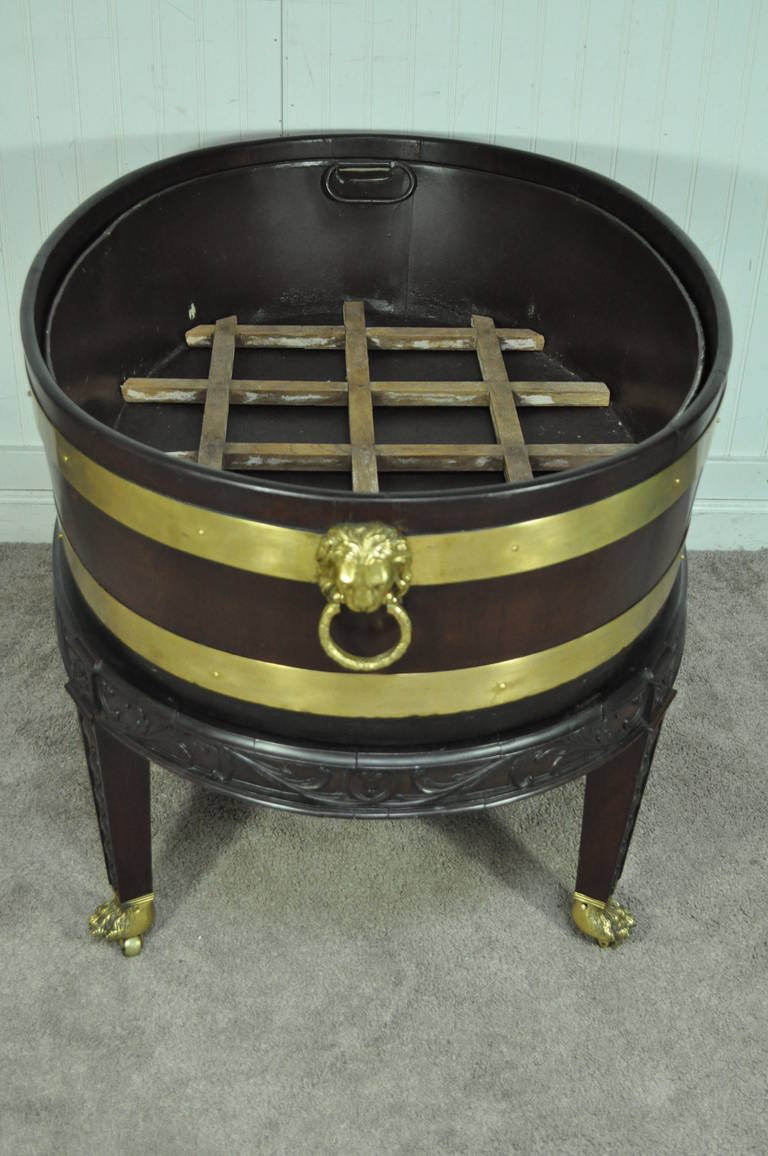 Remarkable 19th century, Brass Bound, Solid Mahogany English George III style Wine Cooler on Rolling Base. This stunning piece features a brass bound mahogany tub with solid brass lion form handles, removable metal basin insert with wooden slotted