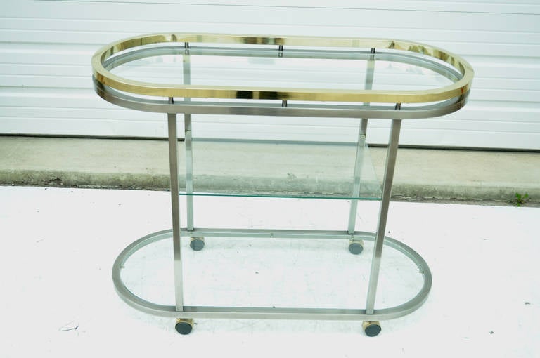 Unique Vintage Modern Brass and Satin Finish Chrome Bar Cart by Design Institute of America (DIA) with the design attributed to Milo Baughman, circa 1986. Item features three glass shelves, ovoid frame, rolling casters, and satin chrome finished